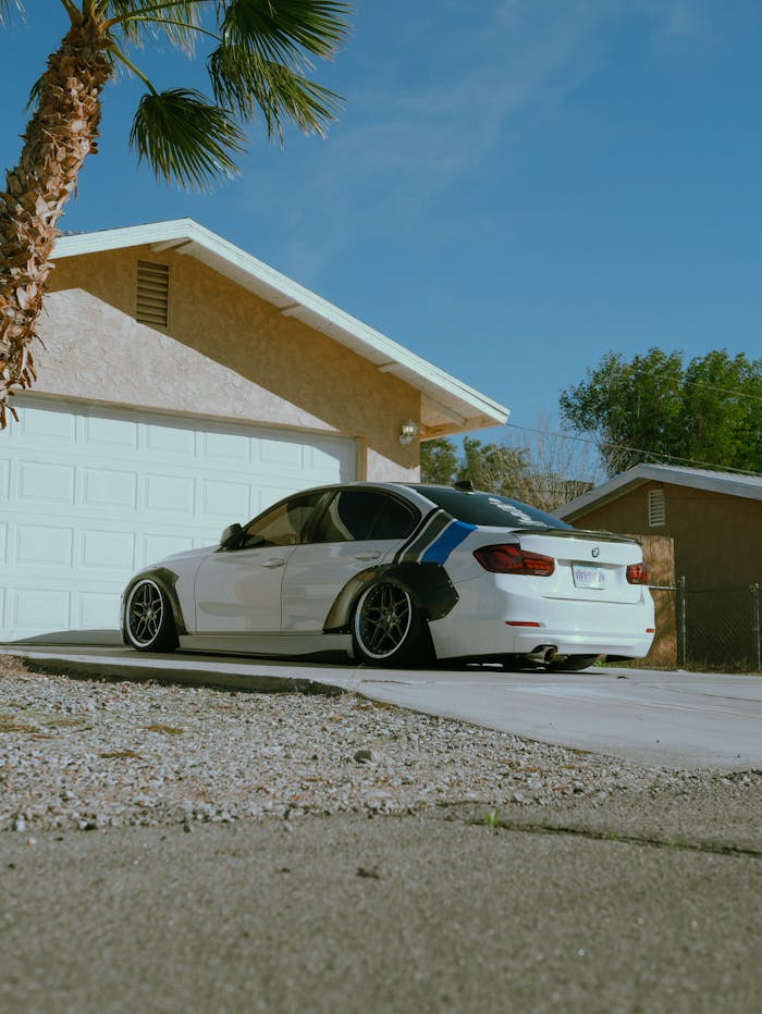portfolio-05 A modern sports car with modifications parked in front of a suburban garage under a clear blue sky.